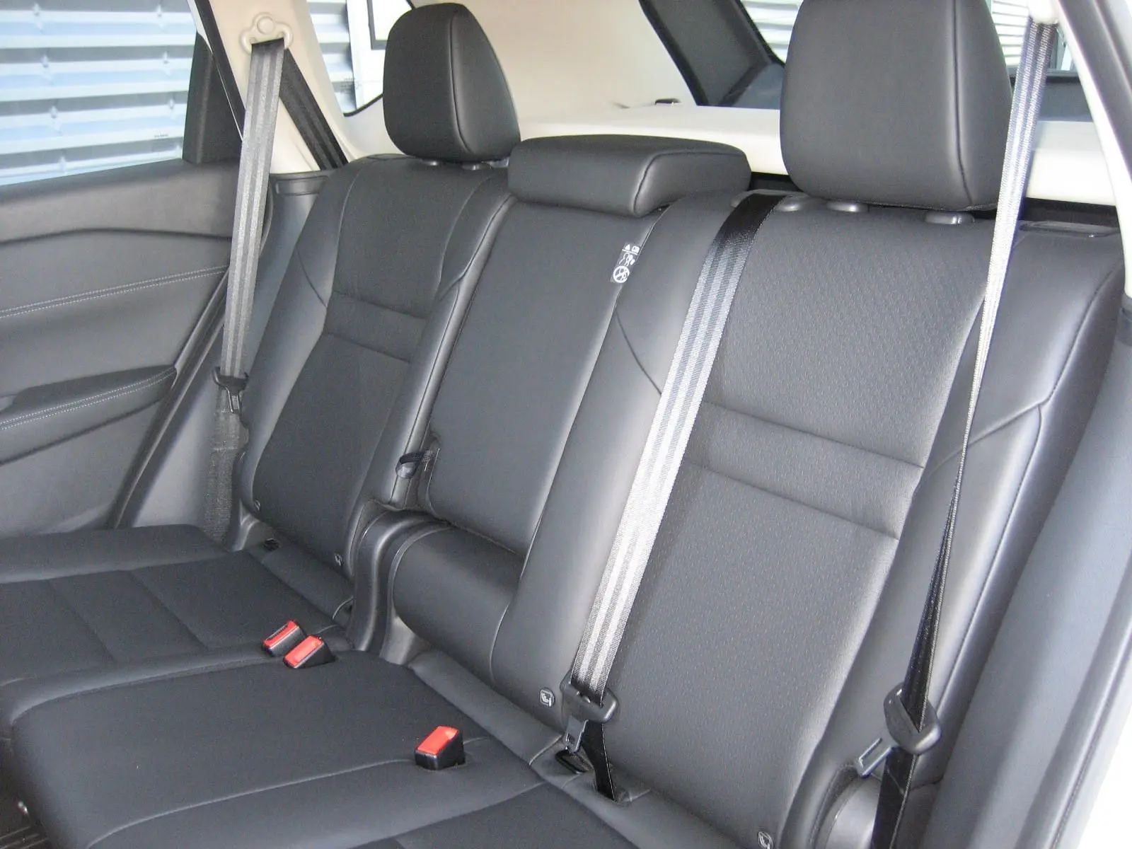 Vue intérieure des sièges arrière en cuir noir du Nissan X-TRAIL blanc nacré, avec ceintures de sécurité visibles.