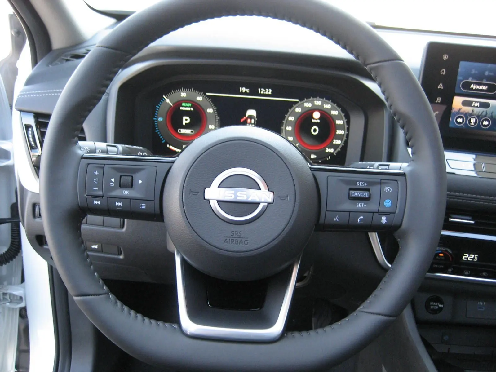 Vue rapprochée du volant noir du Nissan X-TRAIL blanc nacré 2026 avec tableau de bord numérique et écran central tactile.
