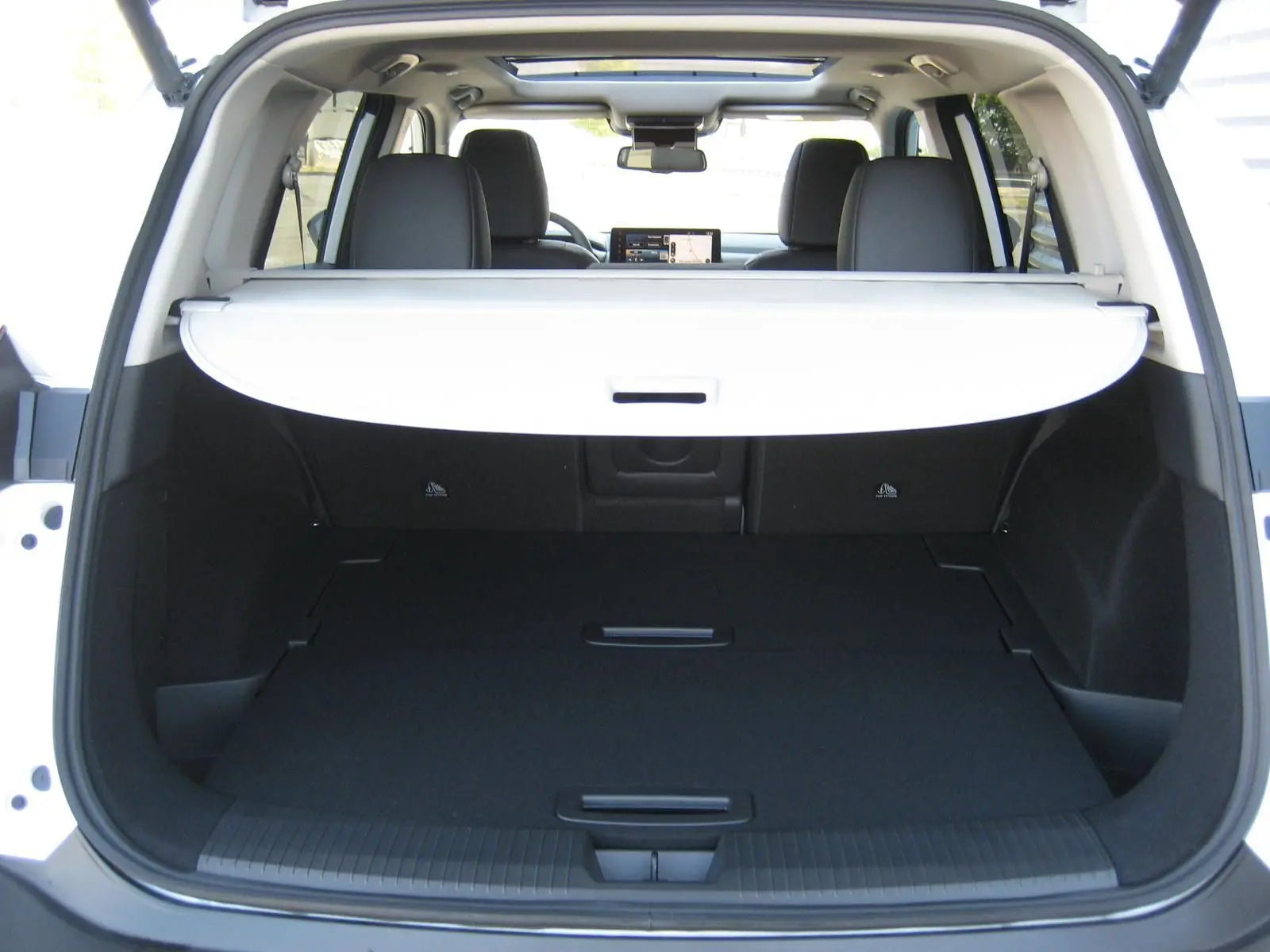 Coffre ouvert vu de l'arrière d'un Nissan X-Trail blanc nacré avec cache-bagages déployé et intérieur noir.