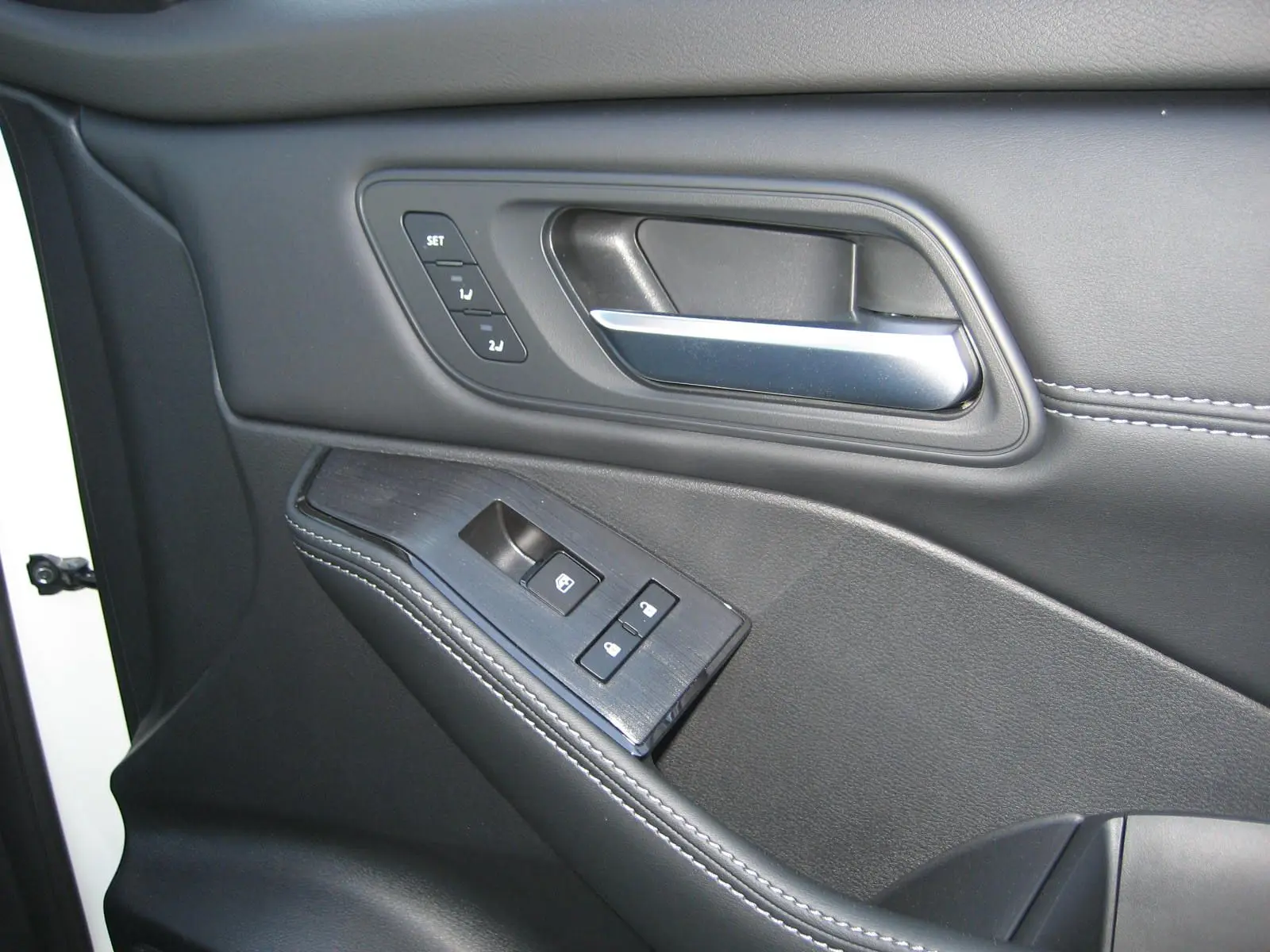 Gros plan sur la porte intérieure côté conducteur du Nissan X-TRAIL blanc nacré, avec commandes de fenêtre et poignée argentée.