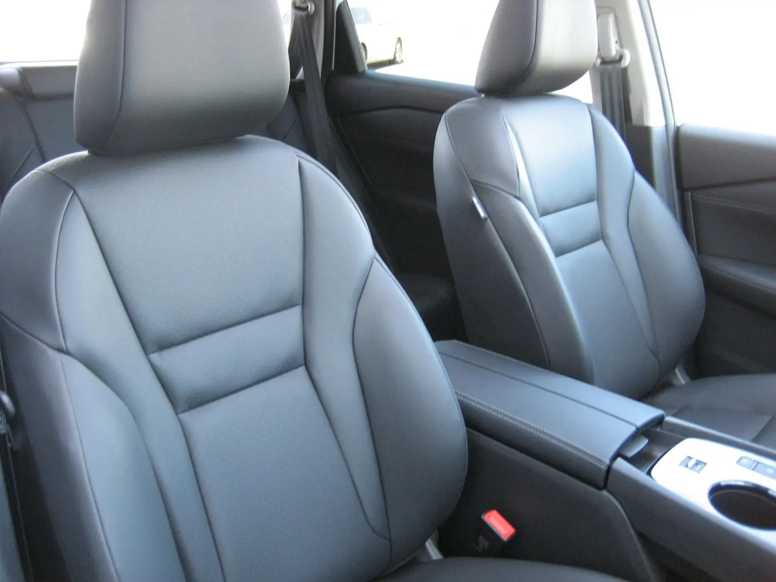 Vue intérieure rapprochée des sièges avant en cuir noir du Nissan X-Trail blanc nacré, avec console centrale visible.
