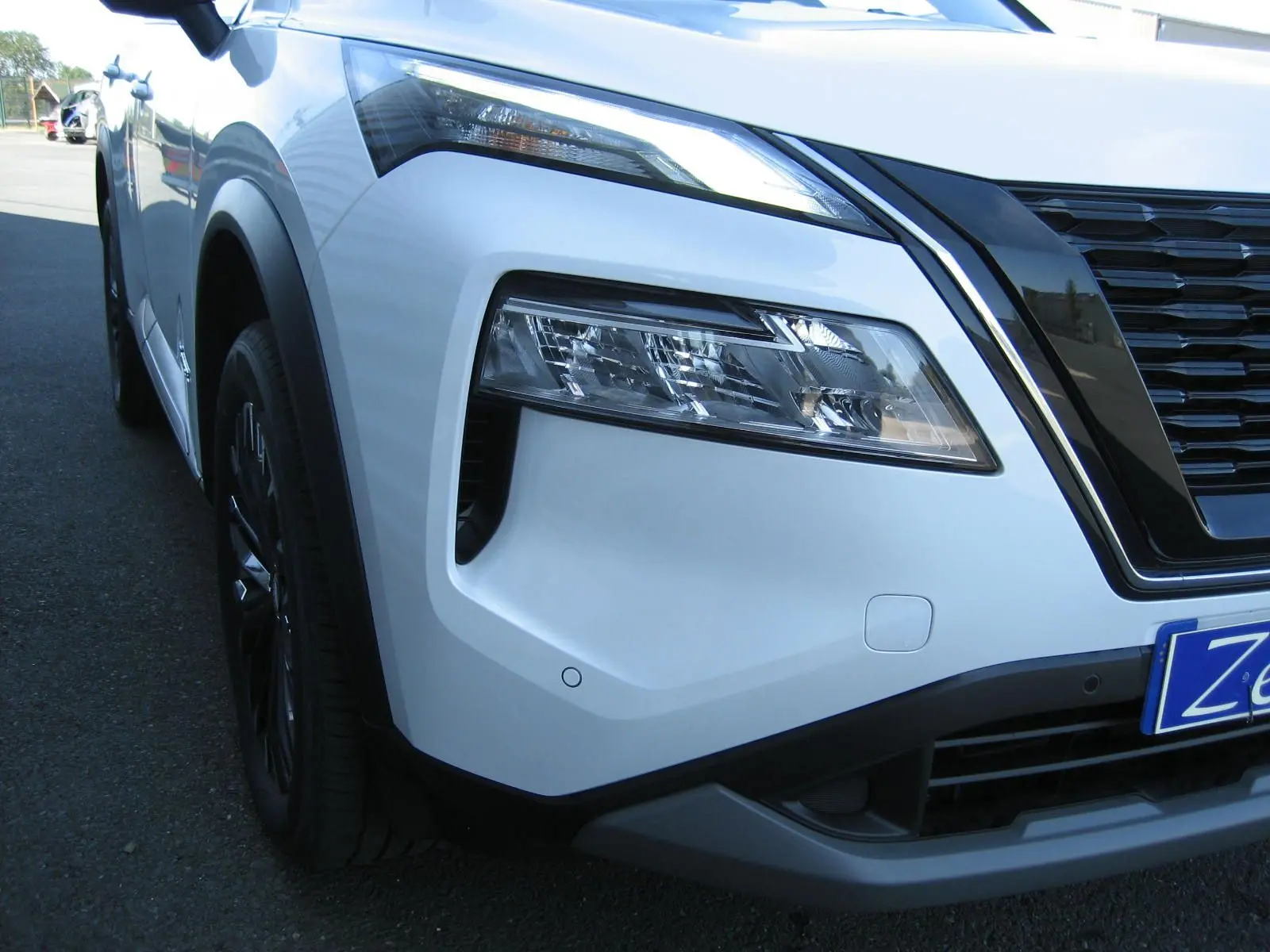 Gros plan sur l'avant droit du Nissan X-Trail blanc nacré, mettant en valeur le phare LED et la calandre noire.