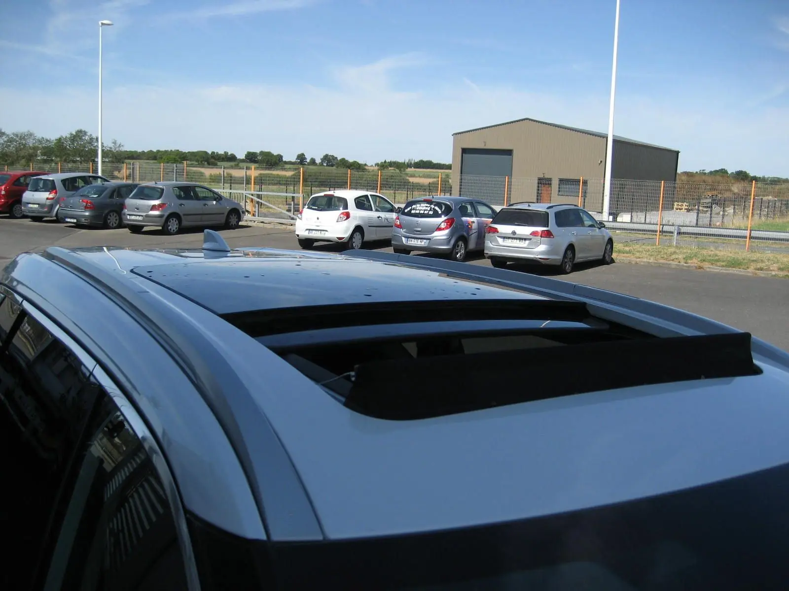 Toit ouvrant ouvert vu de dessus sur un Nissan X-TRAIL blanc nacré, avec barres de toit et antenne requin.