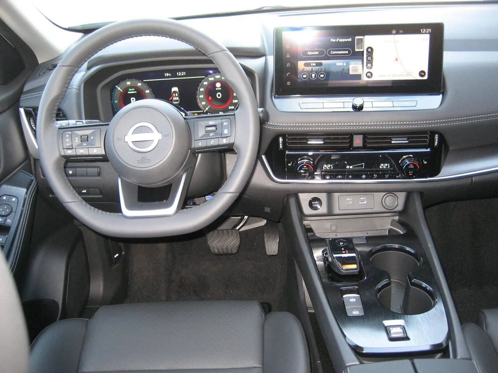 Vue intérieure avant du tableau de bord et volant du Nissan X-TRAIL blanc nacré avec écran tactile et commandes modernes.