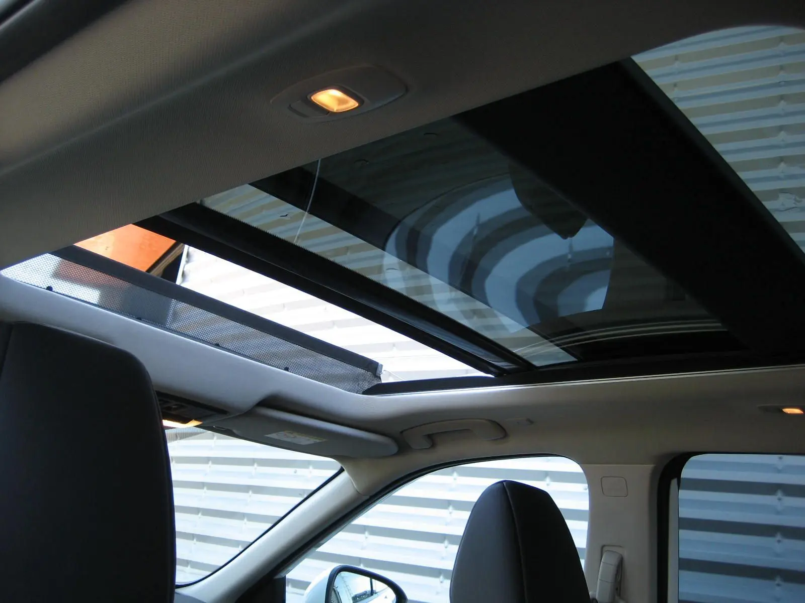Vue intérieure du toit ouvrant panoramique du Nissan X-TRAIL blanc nacré, avec sièges avant et lumière intérieure allumée.