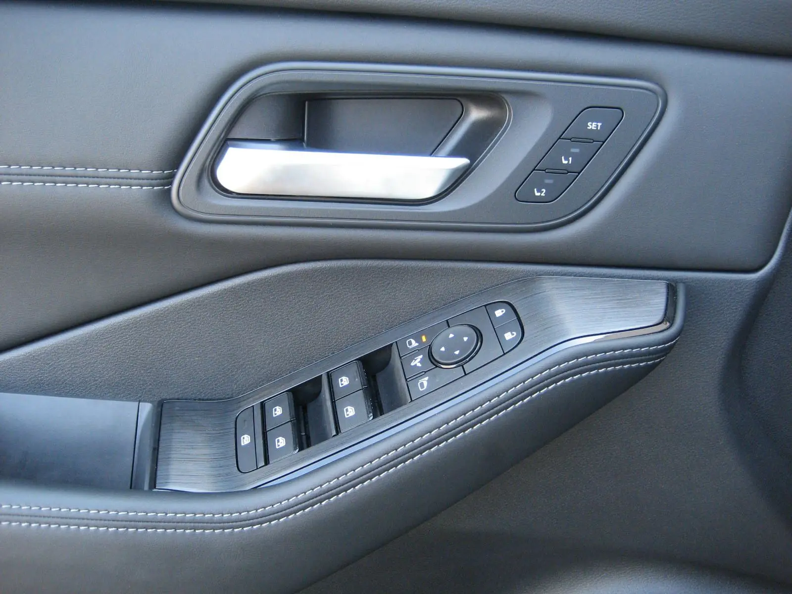 Gros plan sur la poignée intérieure et les commandes de porte en cuir noir avec surpiqûres blanches du Nissan X-Trail blanc nacré.