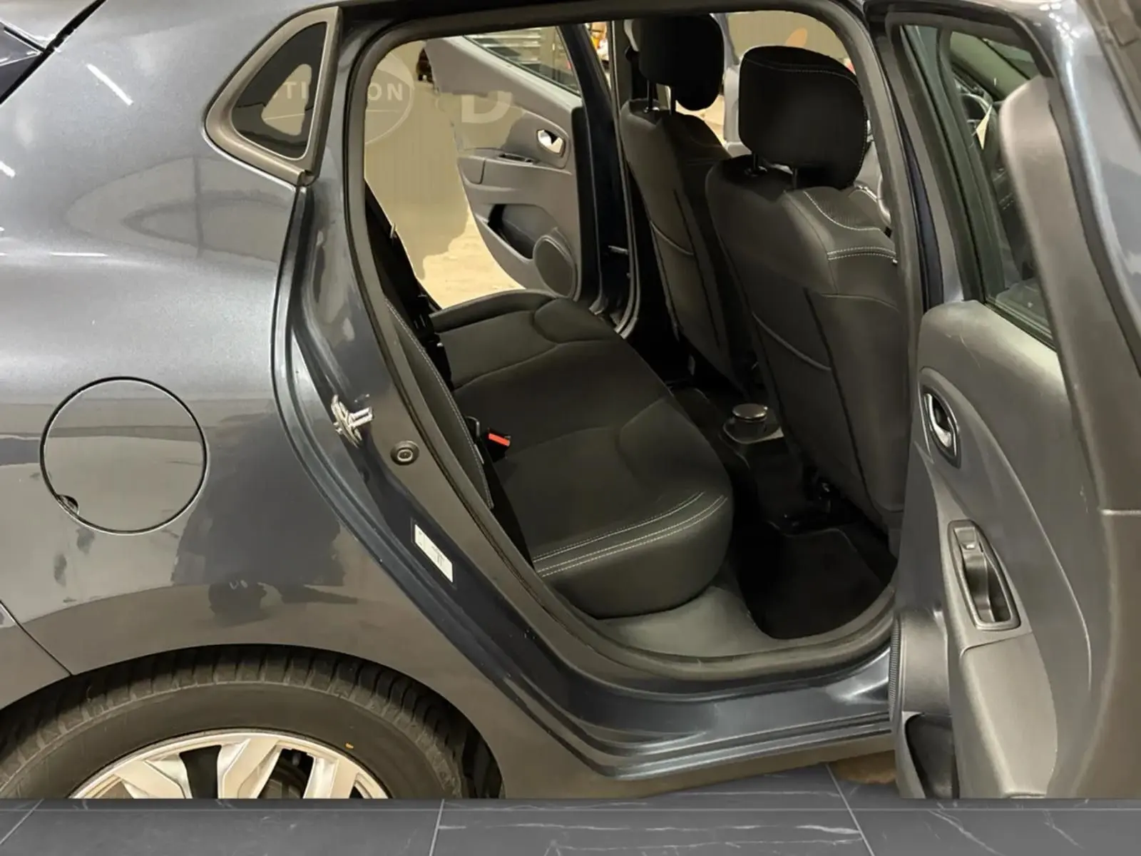 Vue côté gauche arrière de la Renault Clio IV gris foncé métal, porte arrière ouverte dévoilant les sièges arrière en tissu noir.