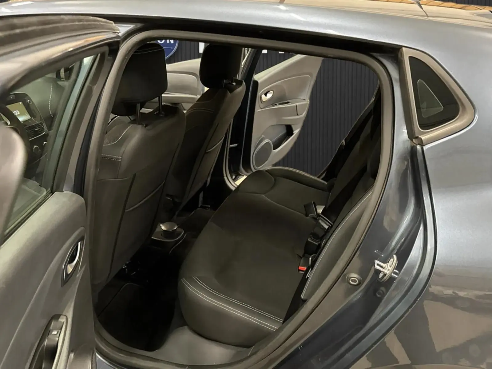 Vue intérieure arrière côté droit de la Renault Clio IV gris foncé métal, montrant les sièges arrière et la portière ouverte.
