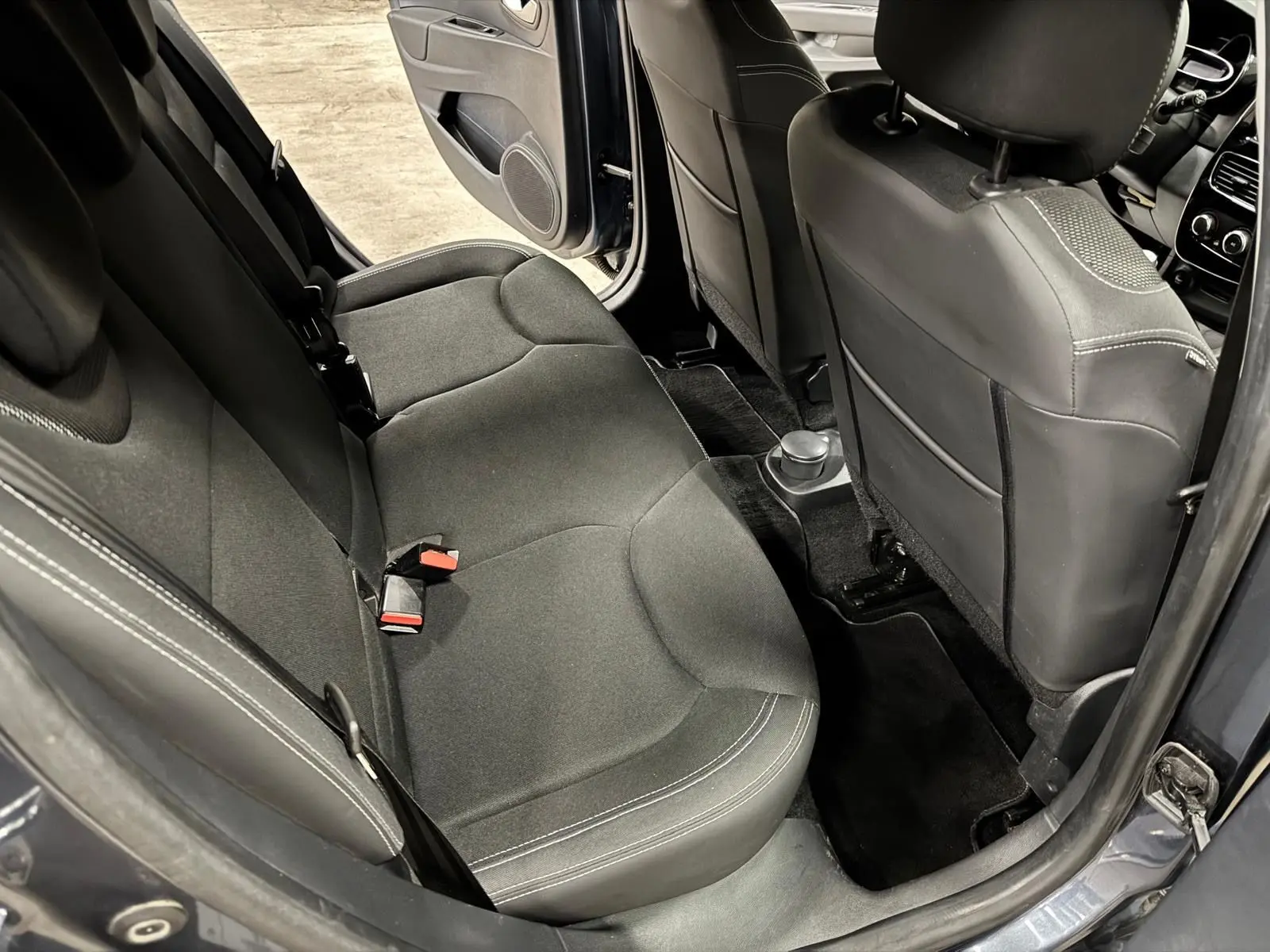 Vue intérieure arrière gauche de la Renault Clio IV gris foncé, montrant les sièges arrière en tissu noir et la porte ouverte.
