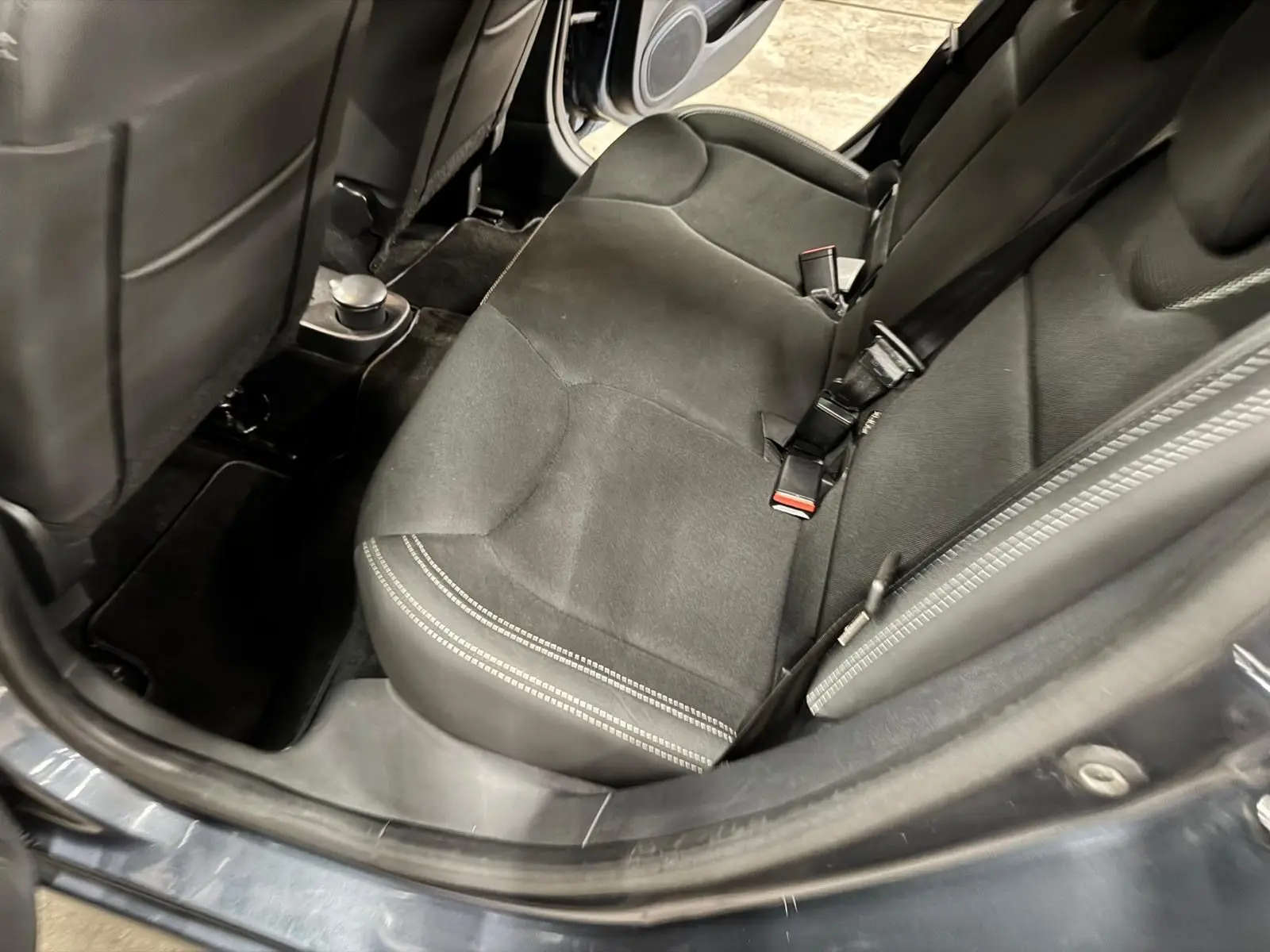Vue intérieure arrière droite montrant la banquette en tissu noir et les ceintures de sécurité d'une Renault Clio IV gris foncé.