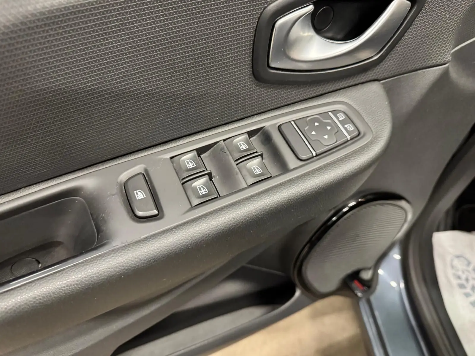 Gros plan sur la commande des vitres électriques côté conducteur de la Renault Clio IV gris foncé métal, porte ouverte.