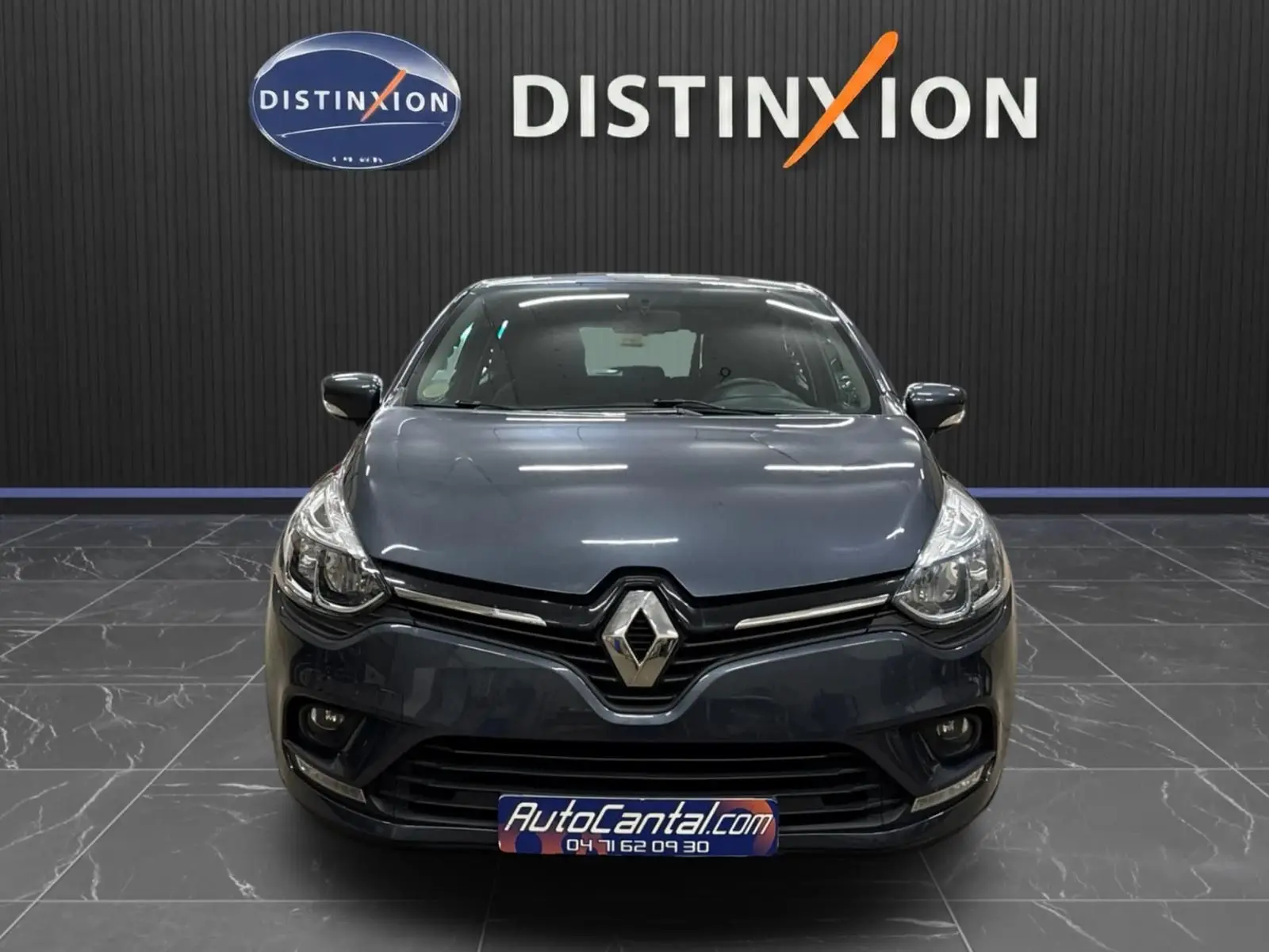 Vue avant d'une Renault Clio IV gris foncé métal, avec logo Renault bien visible et plaque AutoCantal.com.