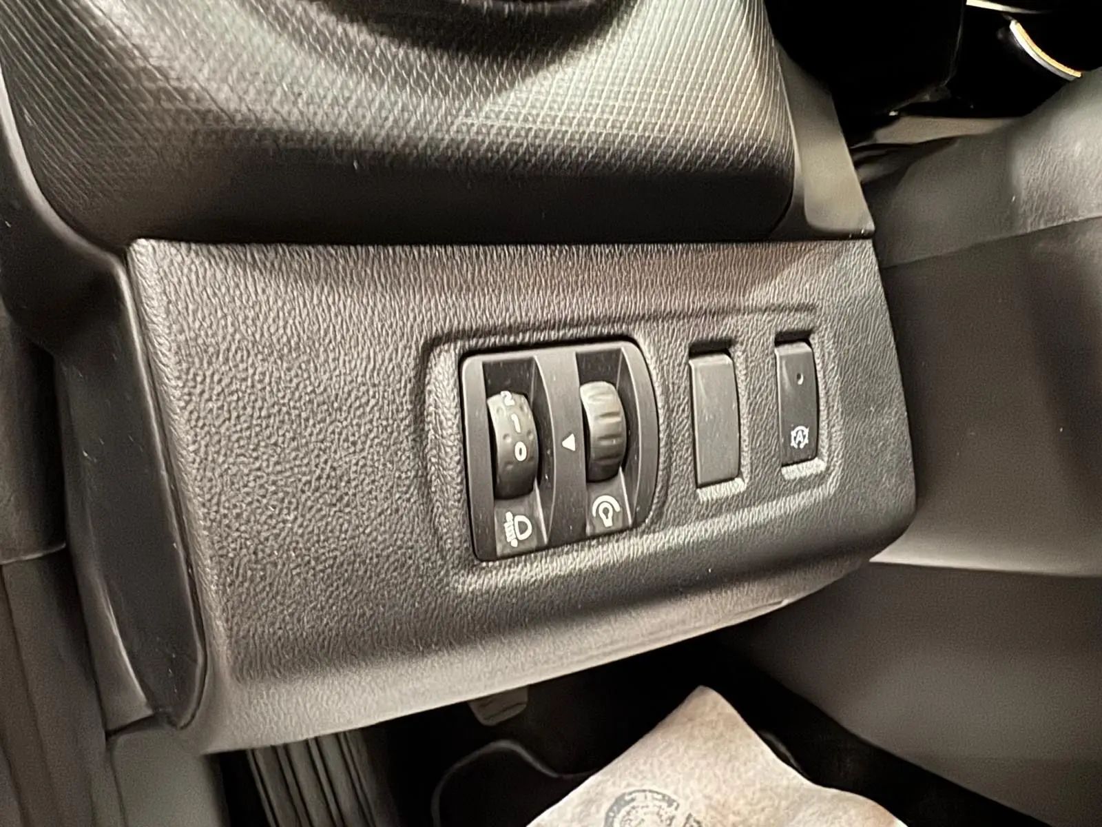 Gros plan sur les commandes d’éclairage et d’assistance au conducteur côté gauche du tableau de bord noir d’une Renault Clio IV gris foncé.