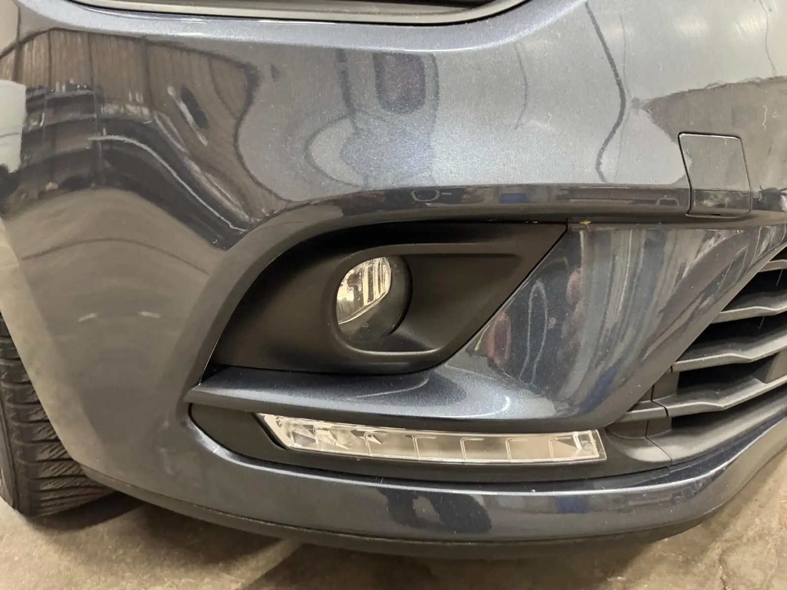 Gros plan sur le pare-chocs avant droit gris foncé métallisé de la Renault Clio IV avec antibrouillard et feux LED intégrés.