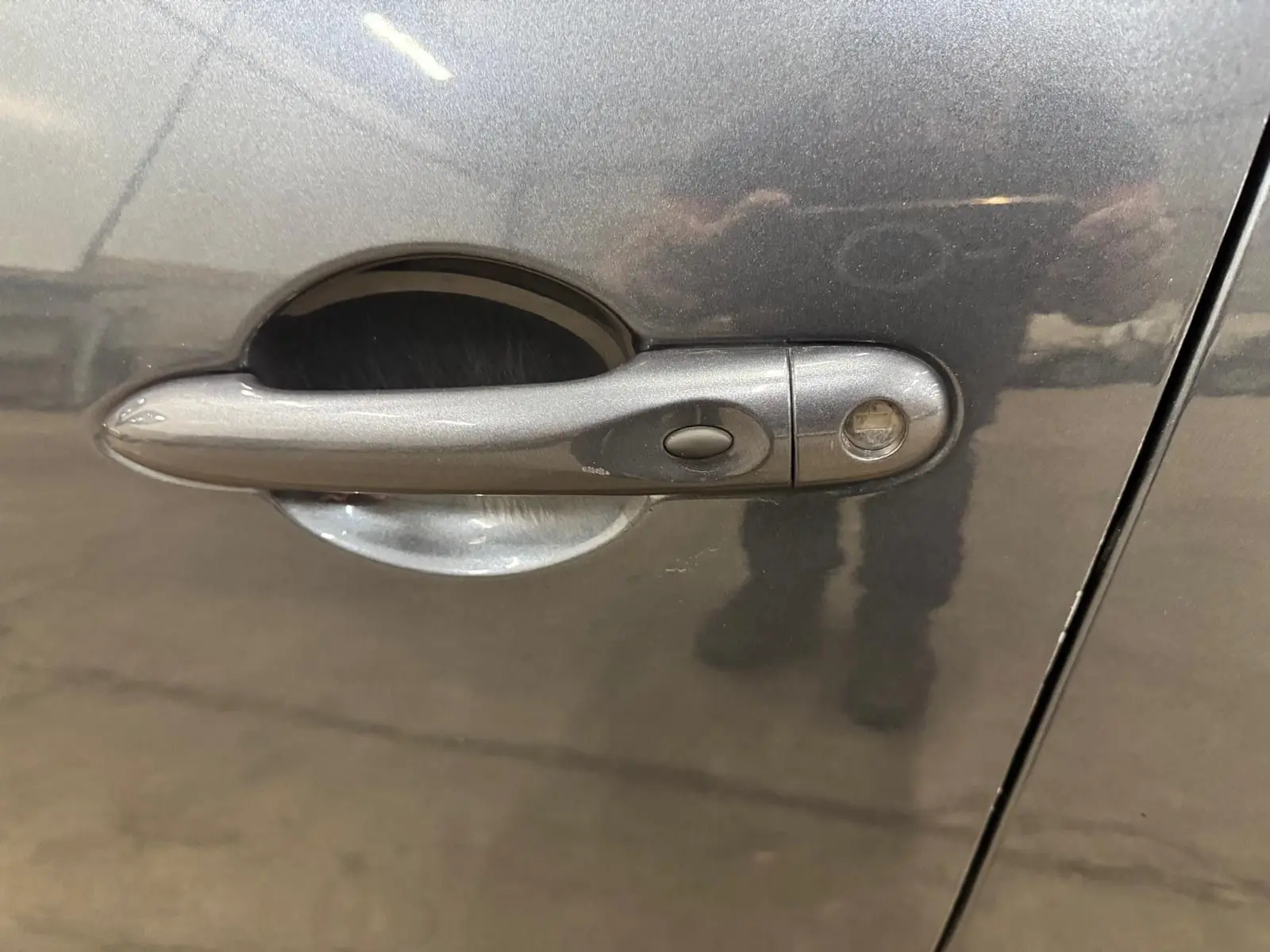 Poignée de porte côté gauche d'une Renault Clio IV gris foncé métallisé avec bouton de verrouillage intégré.