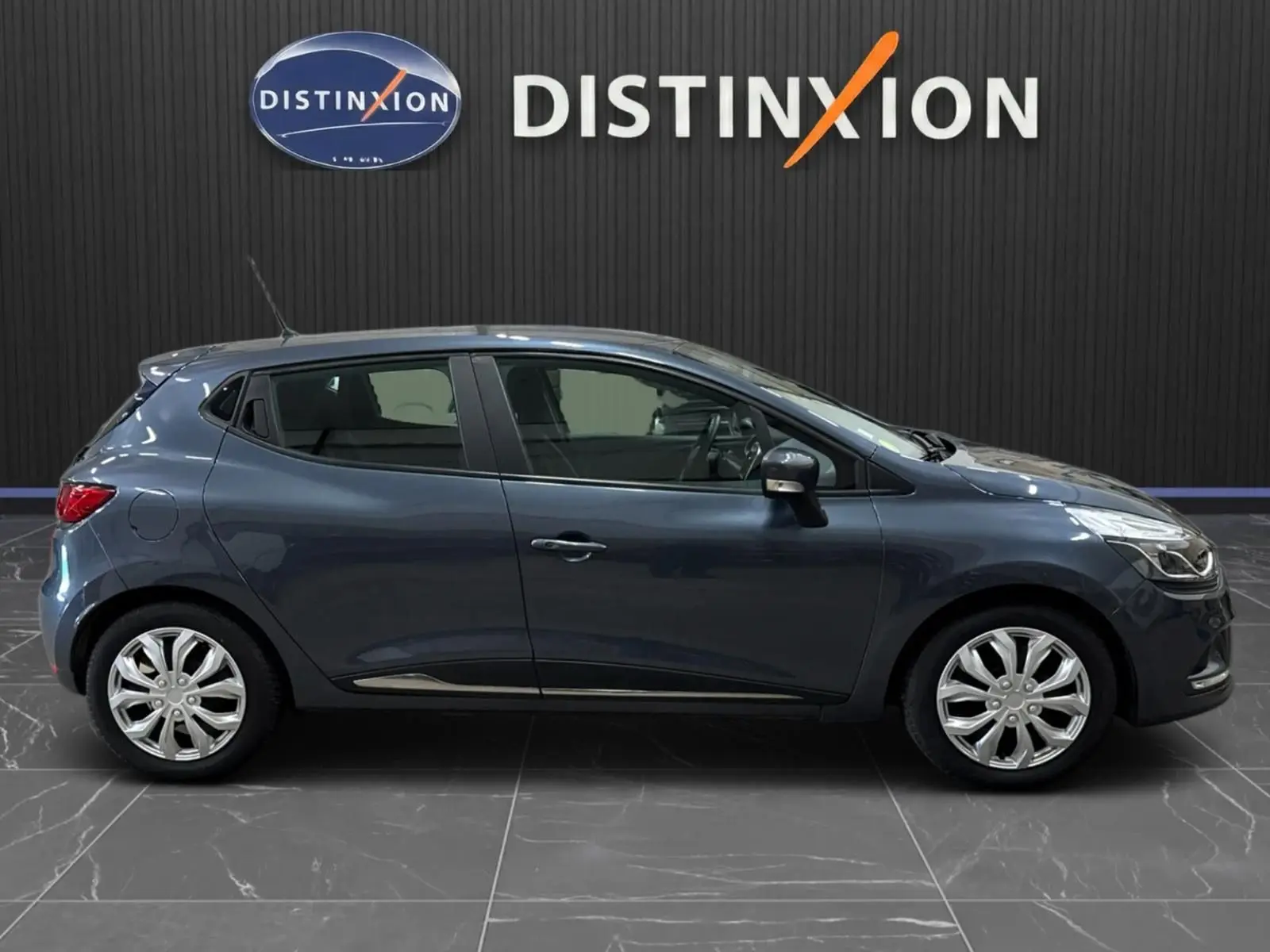 Profil droit d'une Renault Clio IV gris foncé métal, compacte cinq portes, avec jantes alliage et antenne de toit visible.