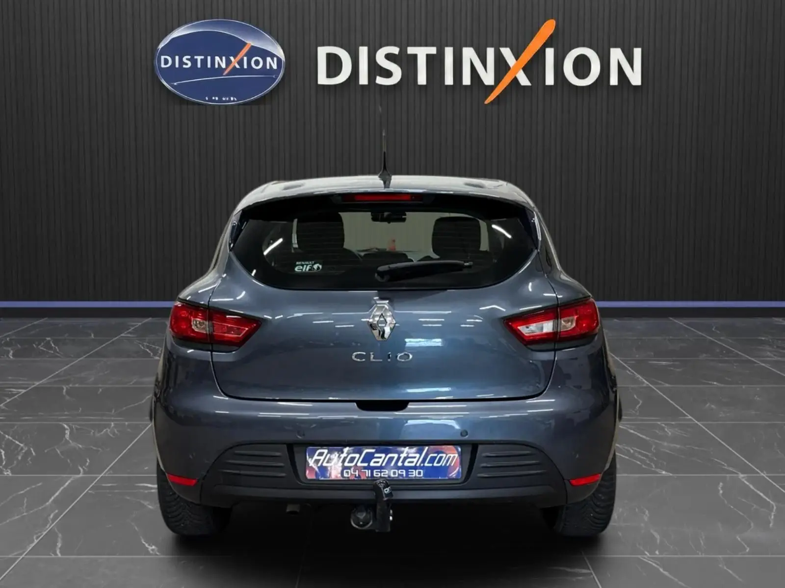 Vue arrière d'une Renault Clio IV gris foncé métal, avec attelage visible et feux rouges allumés.