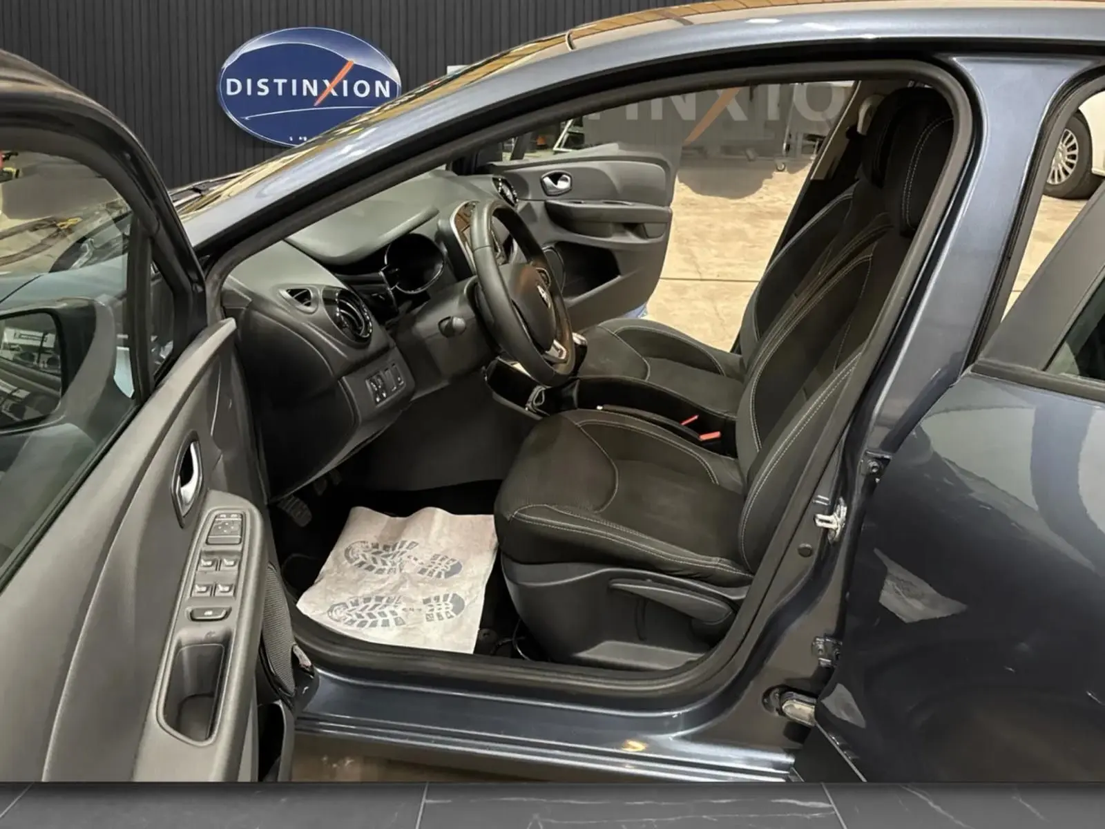 Intérieur côté gauche de la Renault Clio IV gris foncé, avec portes ouvertes et sièges noirs en tissu visibles.