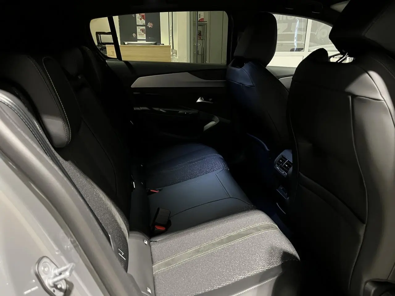 Vue intérieure arrière droite de la Peugeot 308 GT 2024 avec sellerie tri matières noire et surpiqûres vertes.