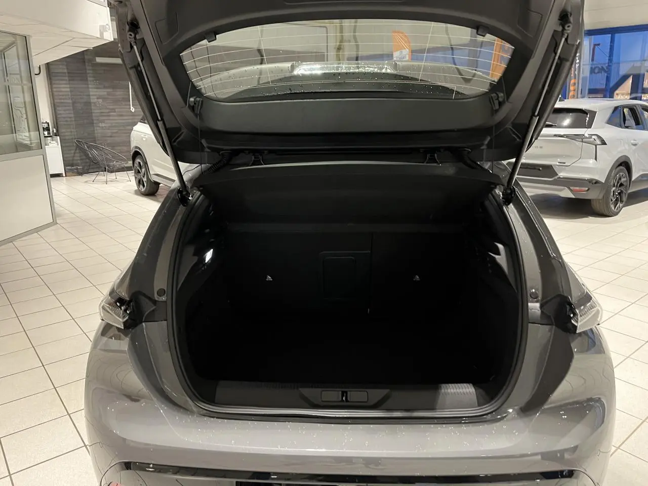 Coffre ouvert vu de l'arrière d'une Peugeot 308 gris selenium avec feux arrière à signature lumineuse griffe à griffe.