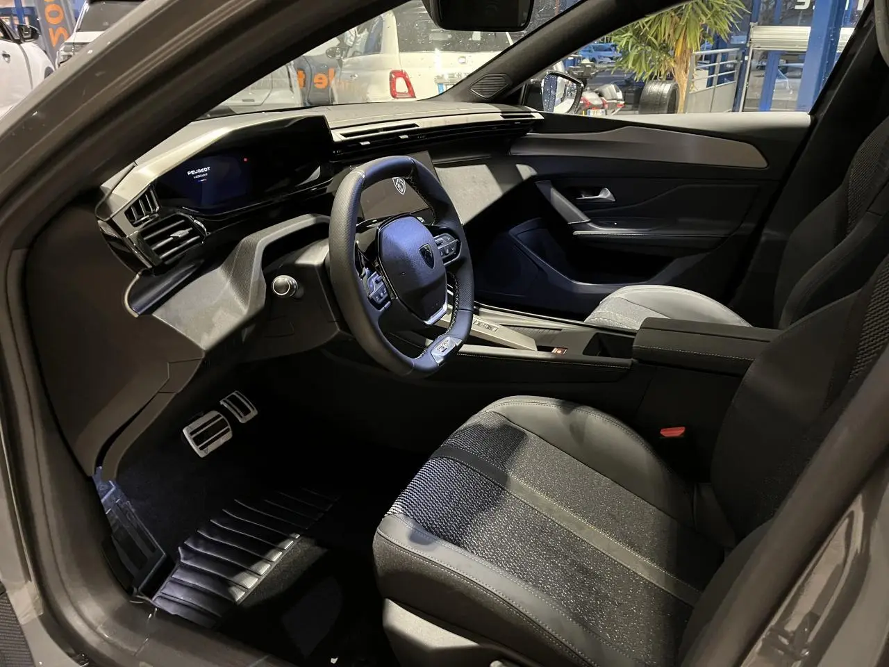 Intérieur avant droit de la Peugeot 308 GT 2024 gris selenium, volant cuir et planche de bord moderne avec écran numérique.