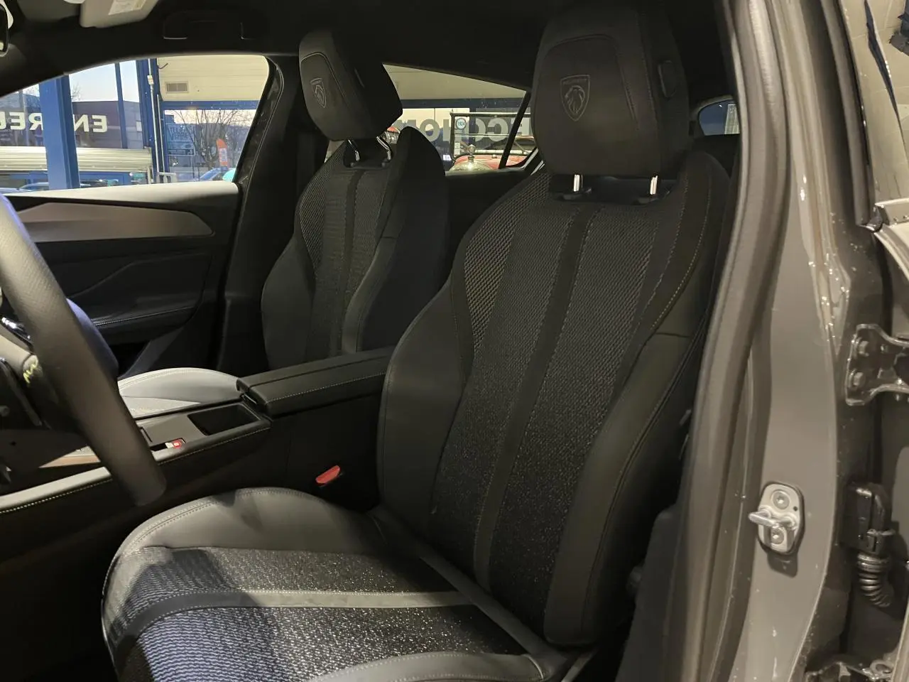 Vue intérieure côté conducteur de la Peugeot 308 GT 2024 gris selenium, sièges sport tri matières avec logo Lion brodé.