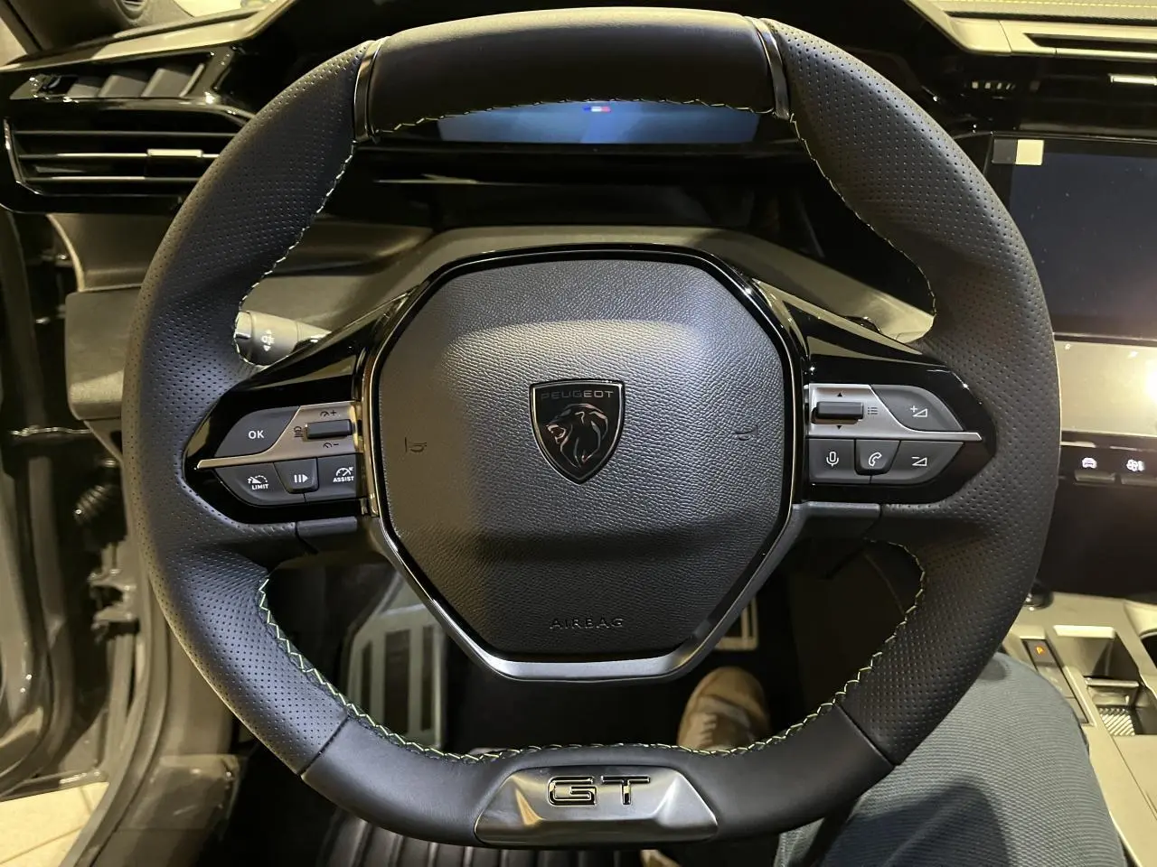 Volant cuir noir avec surpiqûres vertes et logo GT au centre d'une Peugeot 308 Gris Selenium, vue de face intérieure.