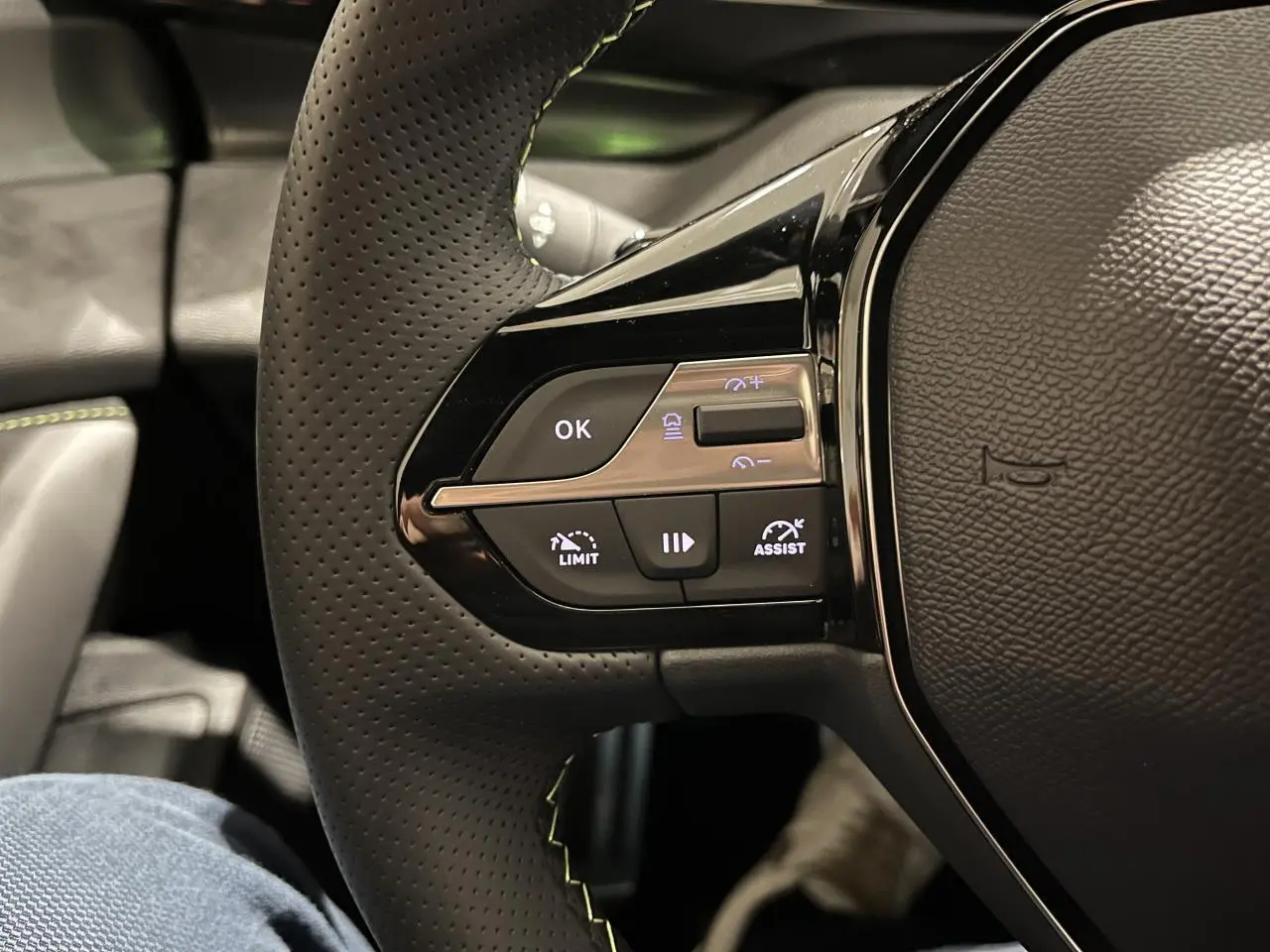 Gros plan sur le volant cuir perforé avec commandes multifonctions et surpiqûres vertes de la Peugeot 308 GT 2024.