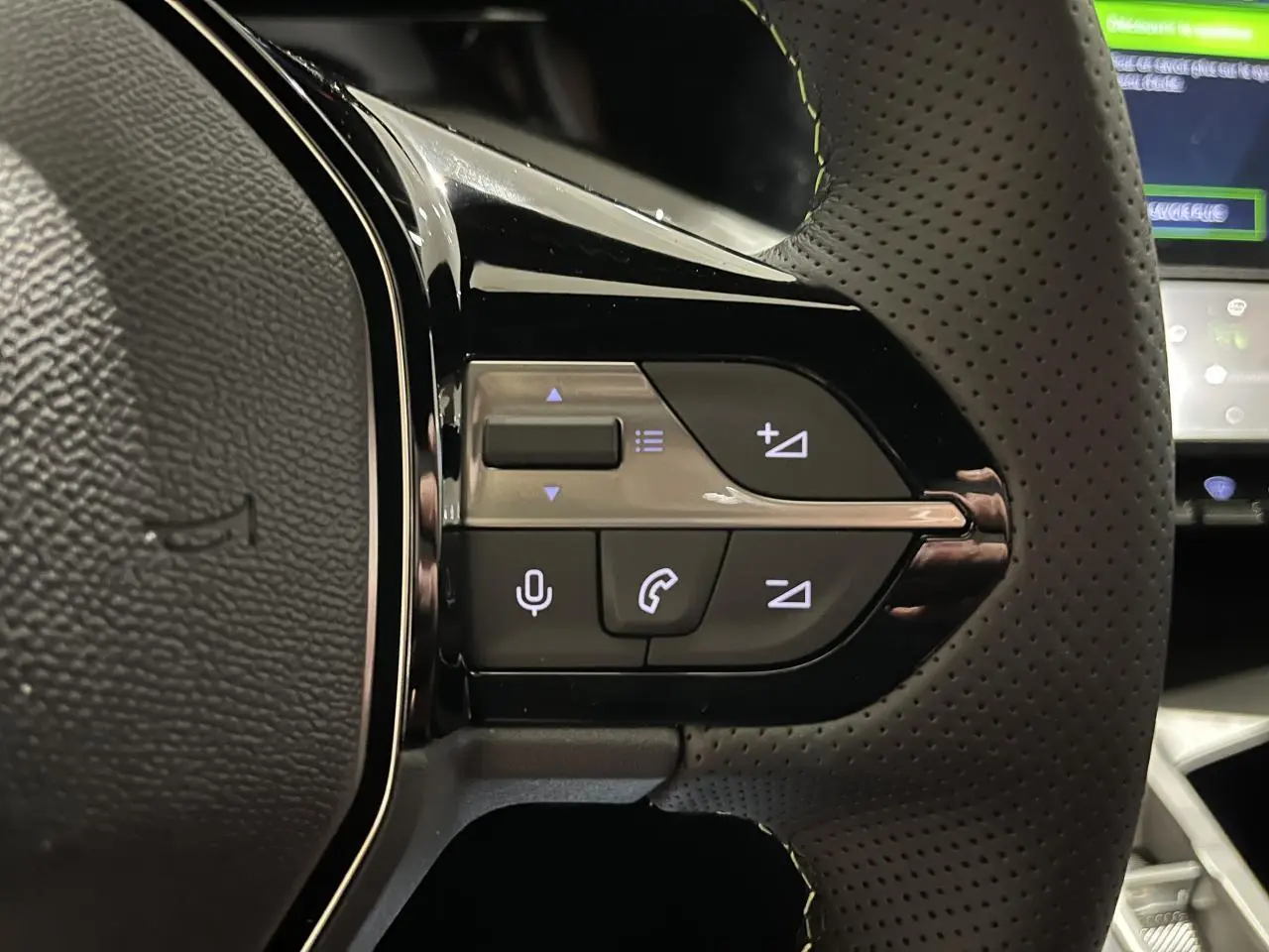 Gros plan sur les commandes gauche du volant cuir perforé de la Peugeot 308 GT 2024 gris selenium.