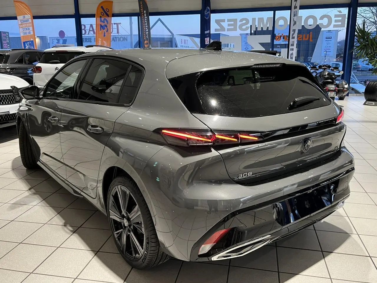 Peugeot 308 gris selenium vue 3/4 arrière droit en showroom, feux arrière LED griffés et jantes alliage 18 pouces.