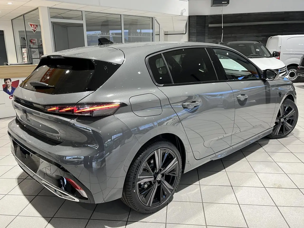 Peugeot 308 GT gris sélénium vue 3/4 arrière droit en intérieur avec jantes alliage noires et feux LED griffés.