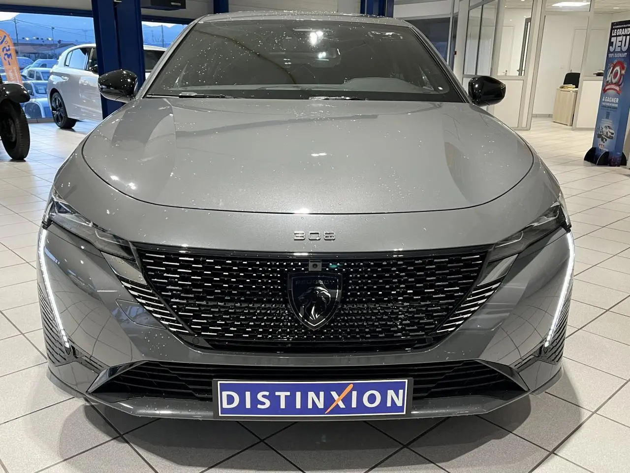 Vue avant d'une Peugeot 308 gris selenium avec calandre noire brillante et feux LED griffés en showroom.