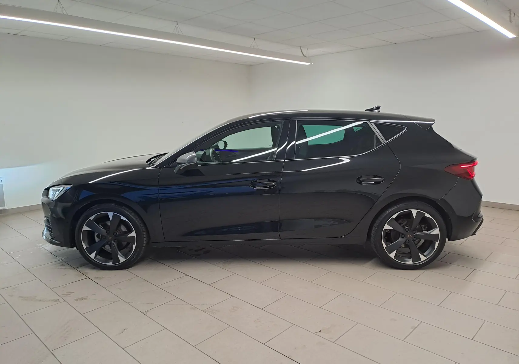 Profil droit de la CUPRA Leon 1.5 TSI 150 DS7 V 2023 en peinture métallisée Noir Minuit, avec jantes noires et grises.
