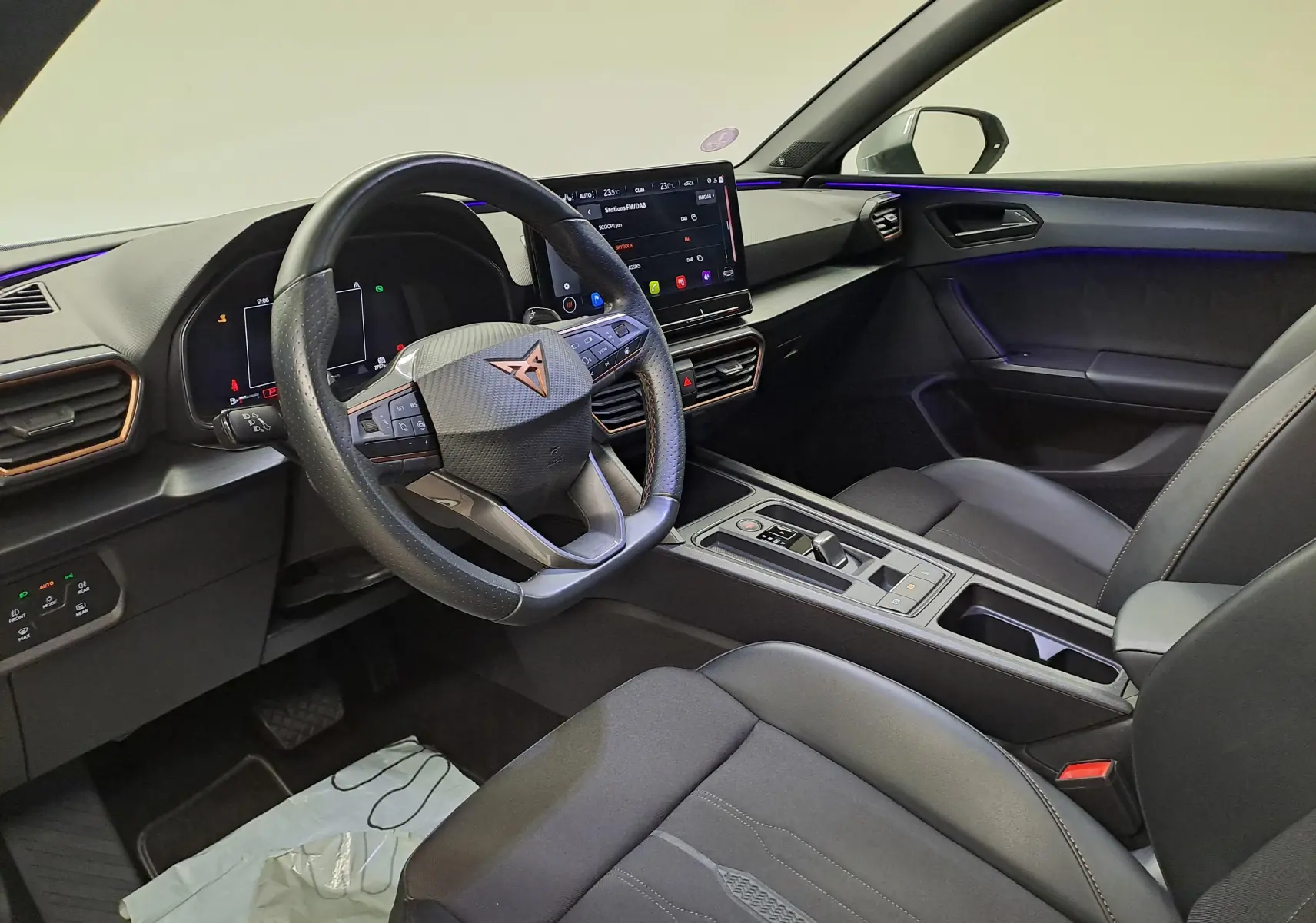 Intérieur avant droit de la CUPRA Leon 2023 noir, avec tableau de bord numérique et éclairage d'ambiance violet.