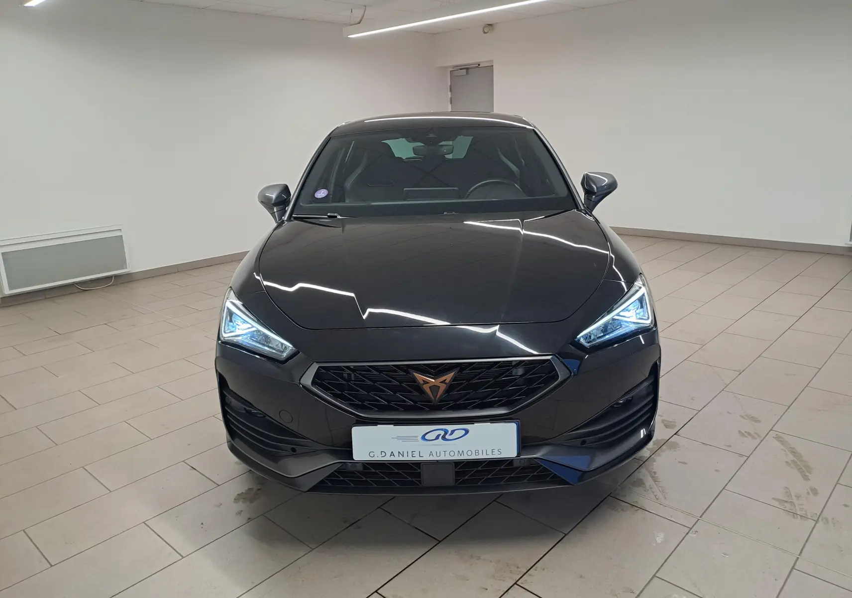 Vue avant d'une CUPRA Leon 1.5 TSI 150 DS7 V noire Minuit avec phares LED allumés dans un showroom.