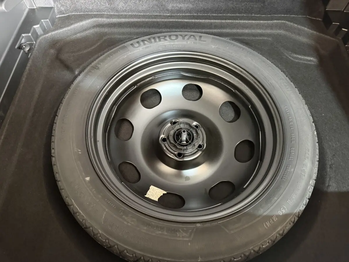 Roue de secours noire Uniroyal dans le coffre d'un Citroën C5 Aircross bleu, vue en plongée.