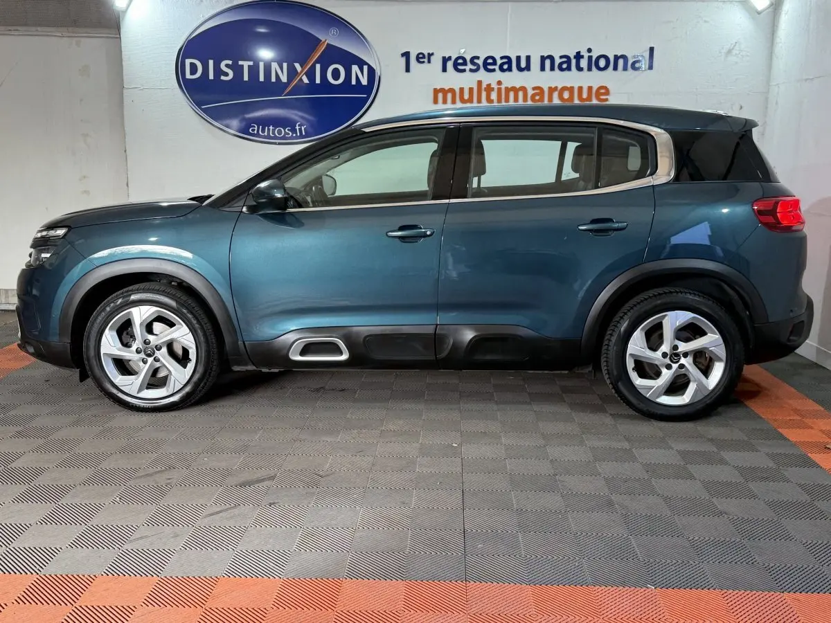 Profil côté gauche d'un Citroën C5 Aircross bleu 2021 en intérieur, avec jantes alliage et barres de toit noires.