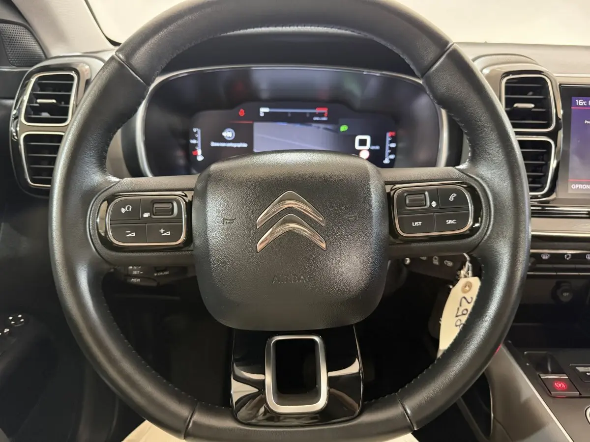 Vue rapprochée du volant cuir noir multifonctions d’un Citroën C5 Aircross 2021 avec tableau de bord numérique en arrière-plan.