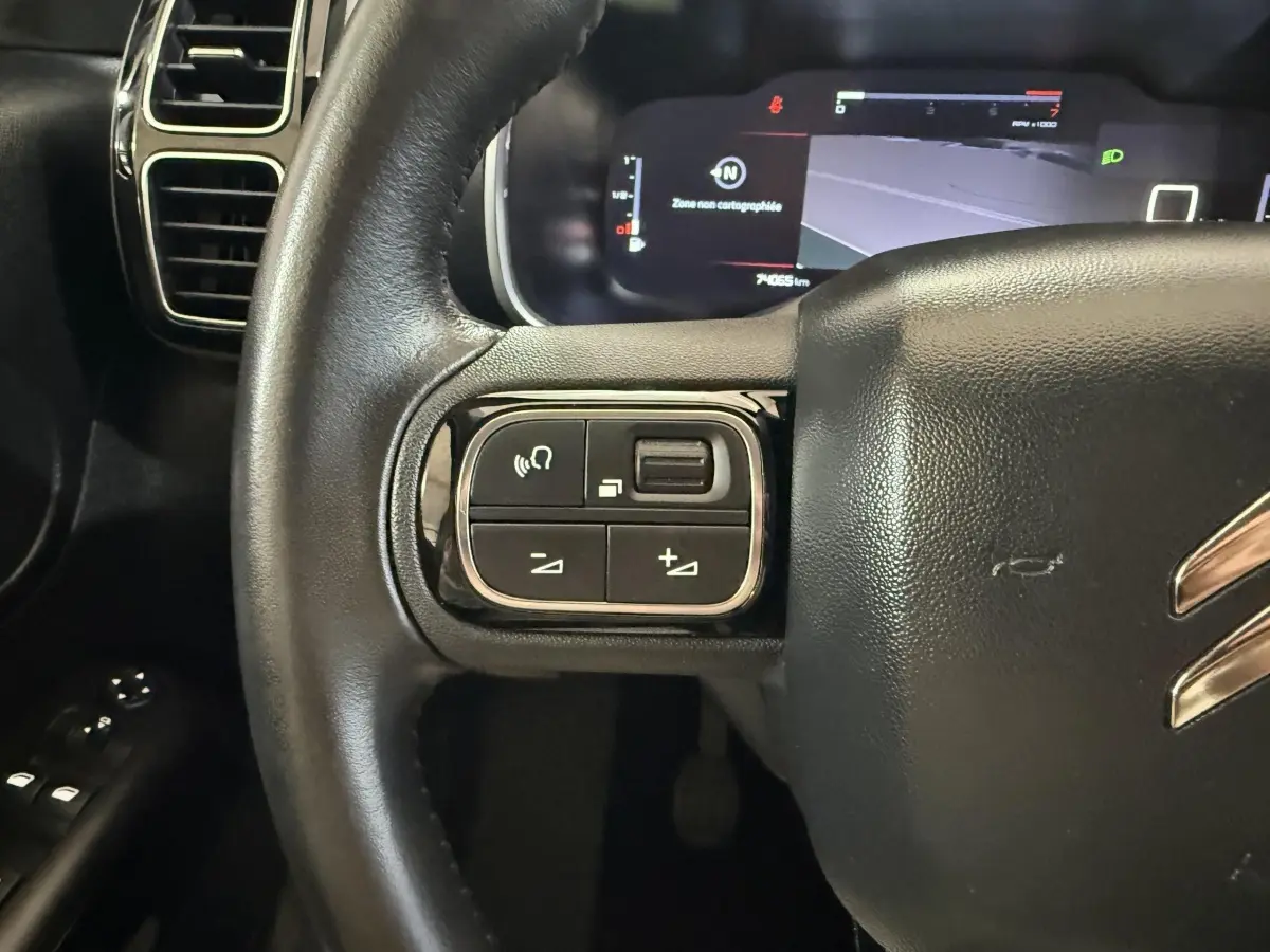 Gros plan sur le volant cuir noir de la Citroën C5 Aircross 2021, avec commandes multifonctions à gauche et tableau de bord numérique.