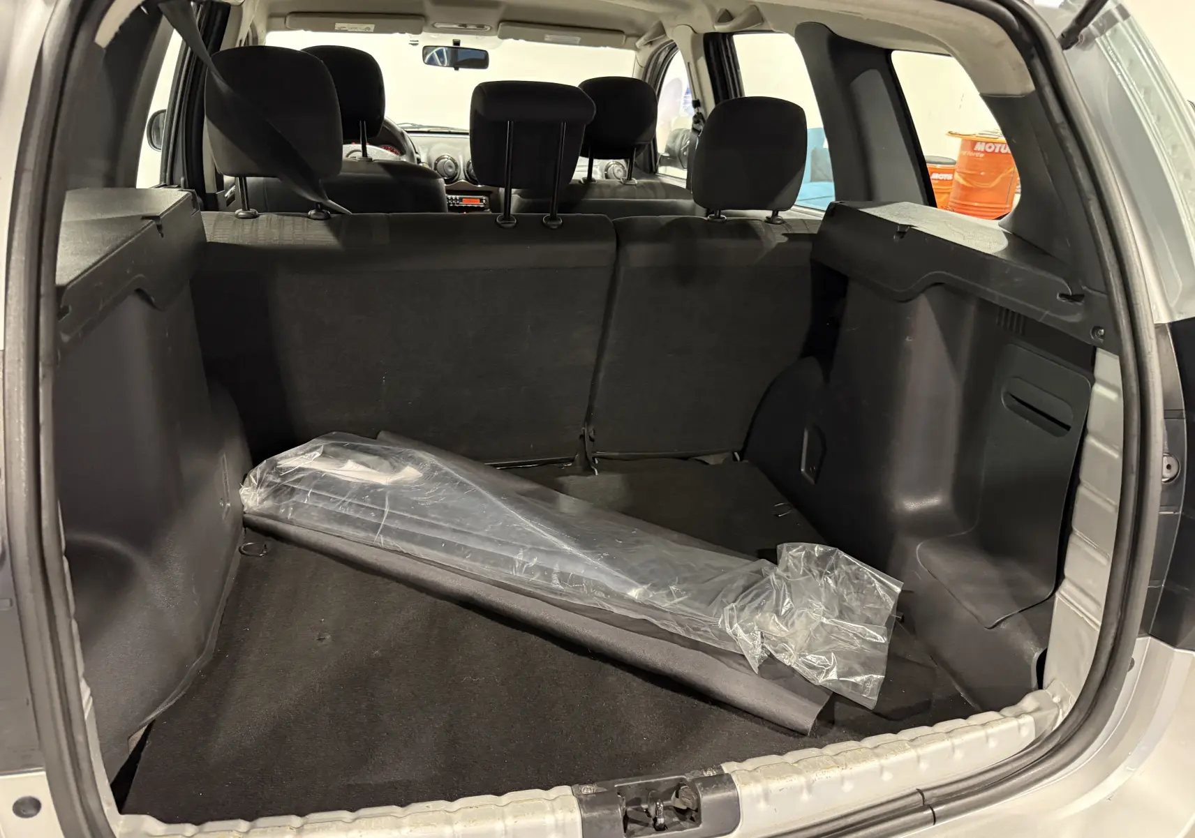 Vue depuis le coffre ouvert du Dacia Duster gris 2011, montrant l’espace de chargement avec un objet emballé en plastique.