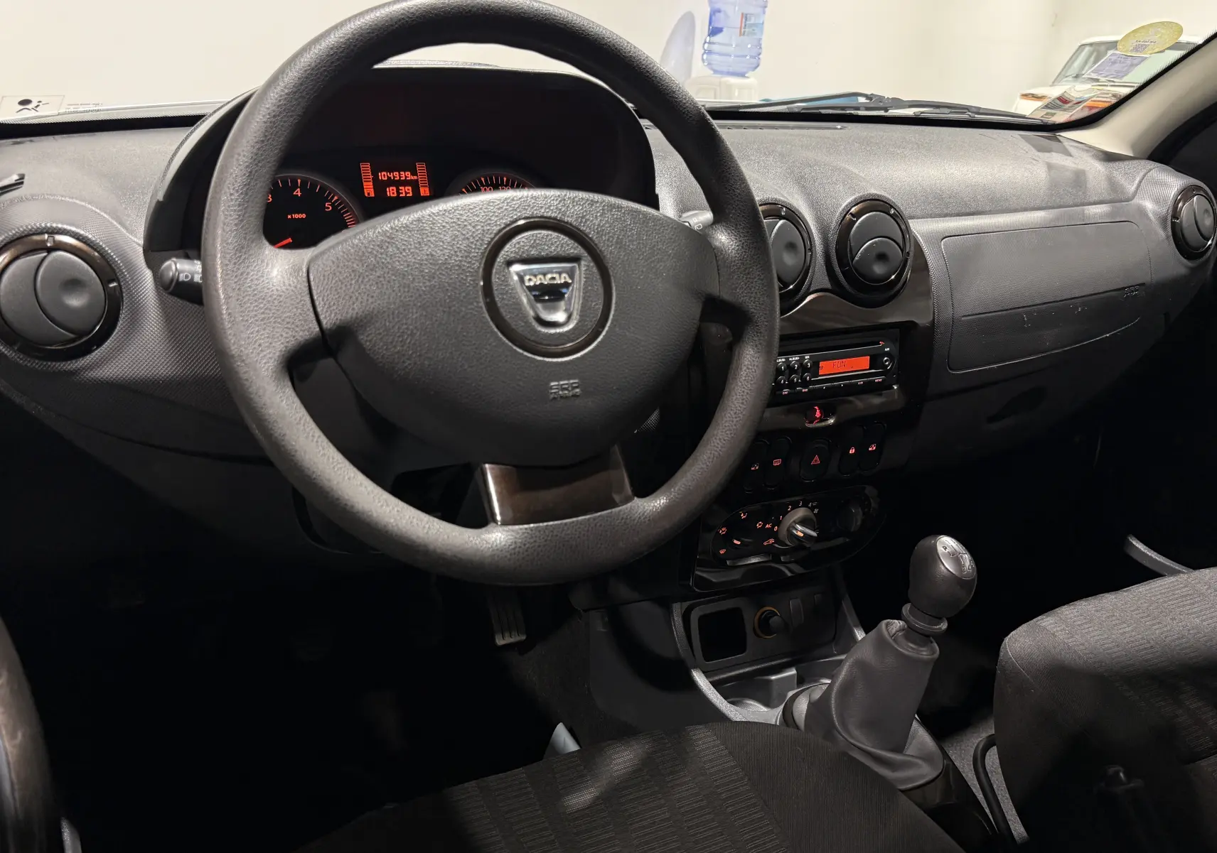 Vue intérieure du tableau de bord et volant noir du Dacia Duster gris, avec levier de vitesses manuel visible.