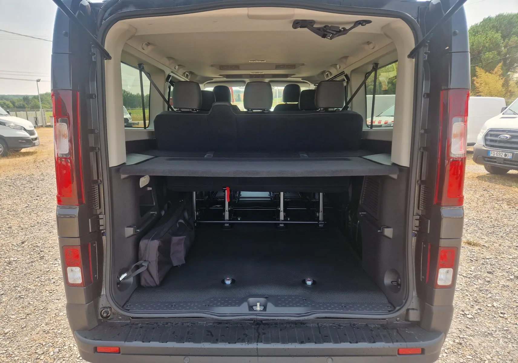 Vue arrière ouverte du Renault Trafic Combi noir 2026, montrant l'espace intérieur avec sièges et fixation pour fauteuil roulant.