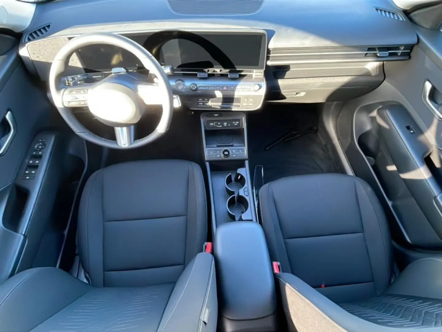 Vue intérieure avant du Hyundai Kona 2025 hybride, sièges noirs, volant multifonction et grand écran numérique.