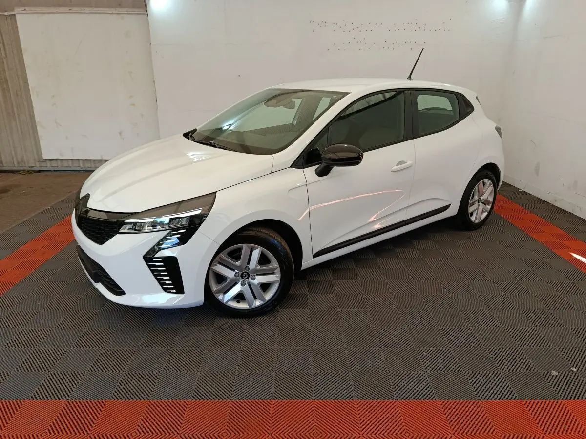 Renault Clio blanche vue 3/4 avant droit en intérieur, avec phares LED et rétroviseurs noirs contrastants.