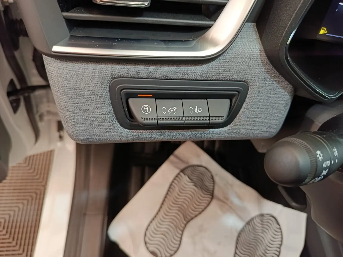 Détail intérieur côté gauche de la planche de bord grise avec commandes de réglage des phares et verrouillage sur Renault Clio blanche.