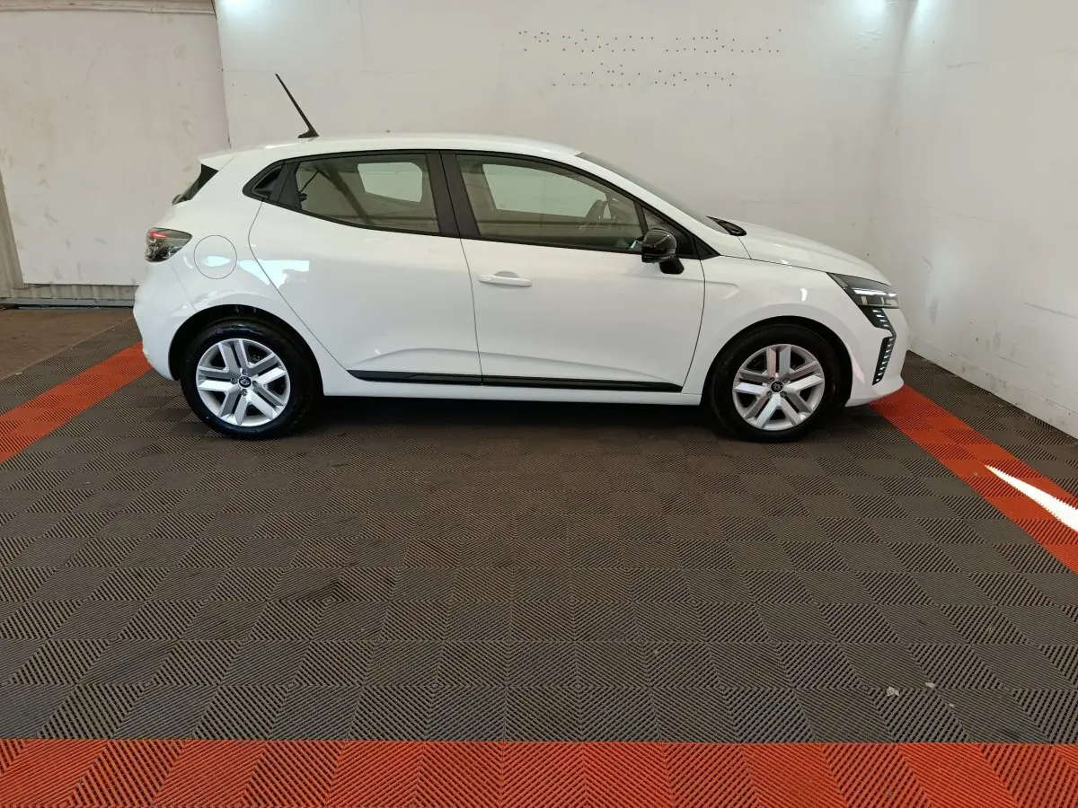Renault Clio blanc vue de profil côté gauche dans un garage avec jantes alliage et feux LED avant allumés.