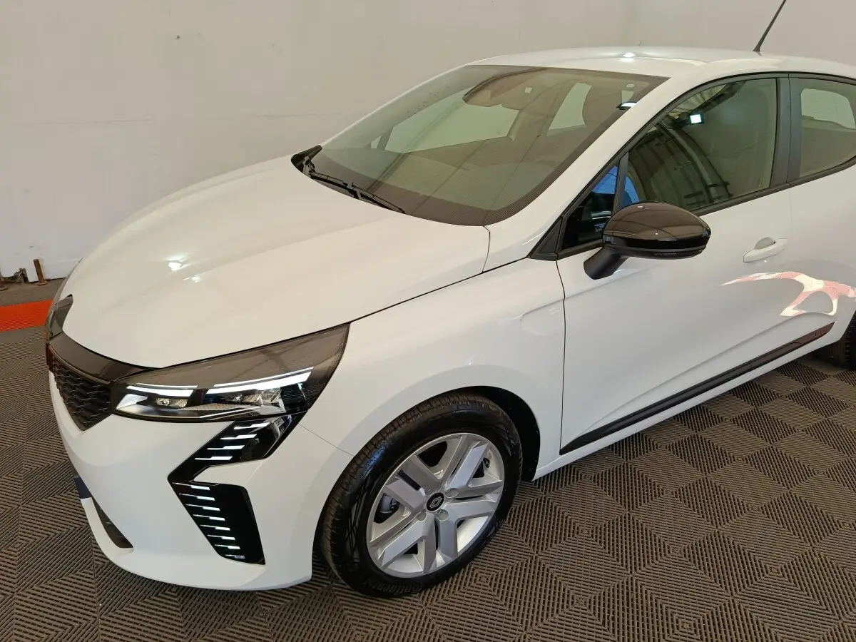 Renault Clio blanche vue 3/4 avant droit, avec phares LED distinctifs et rétroviseur noir brillant.