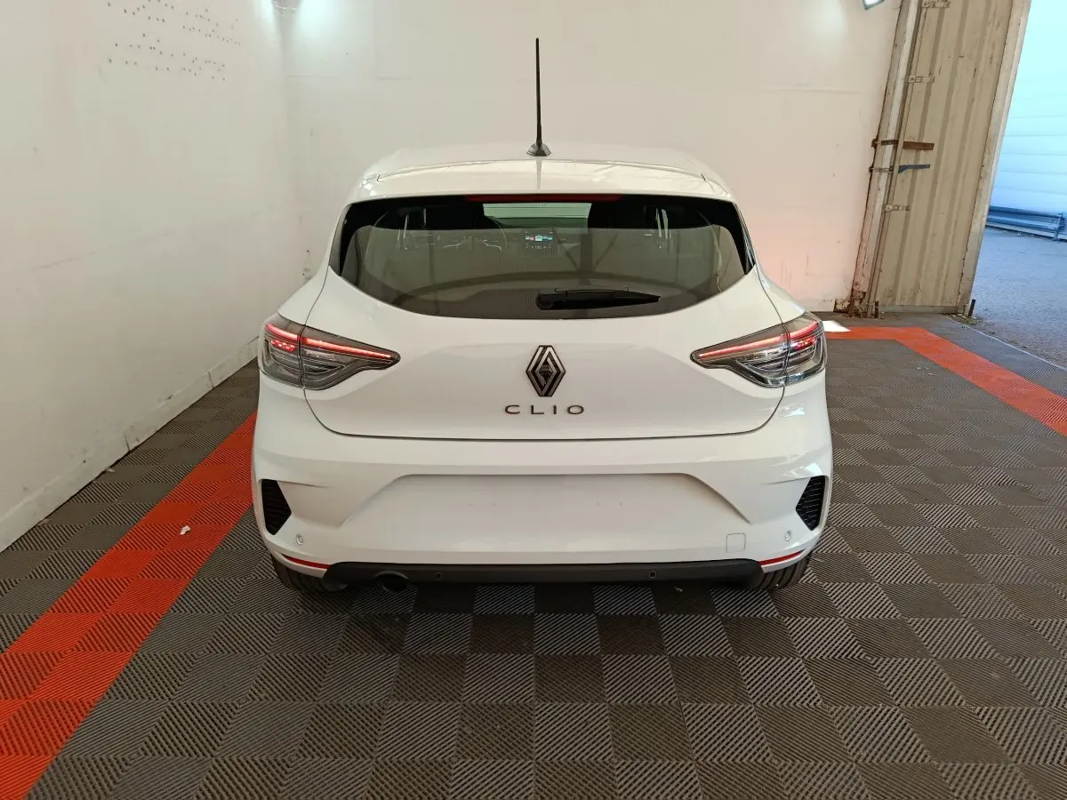 Vue arrière d'une Renault Clio blanche 2024 avec feux LED et logo Renault centré sur un sol à damier gris et rouge.