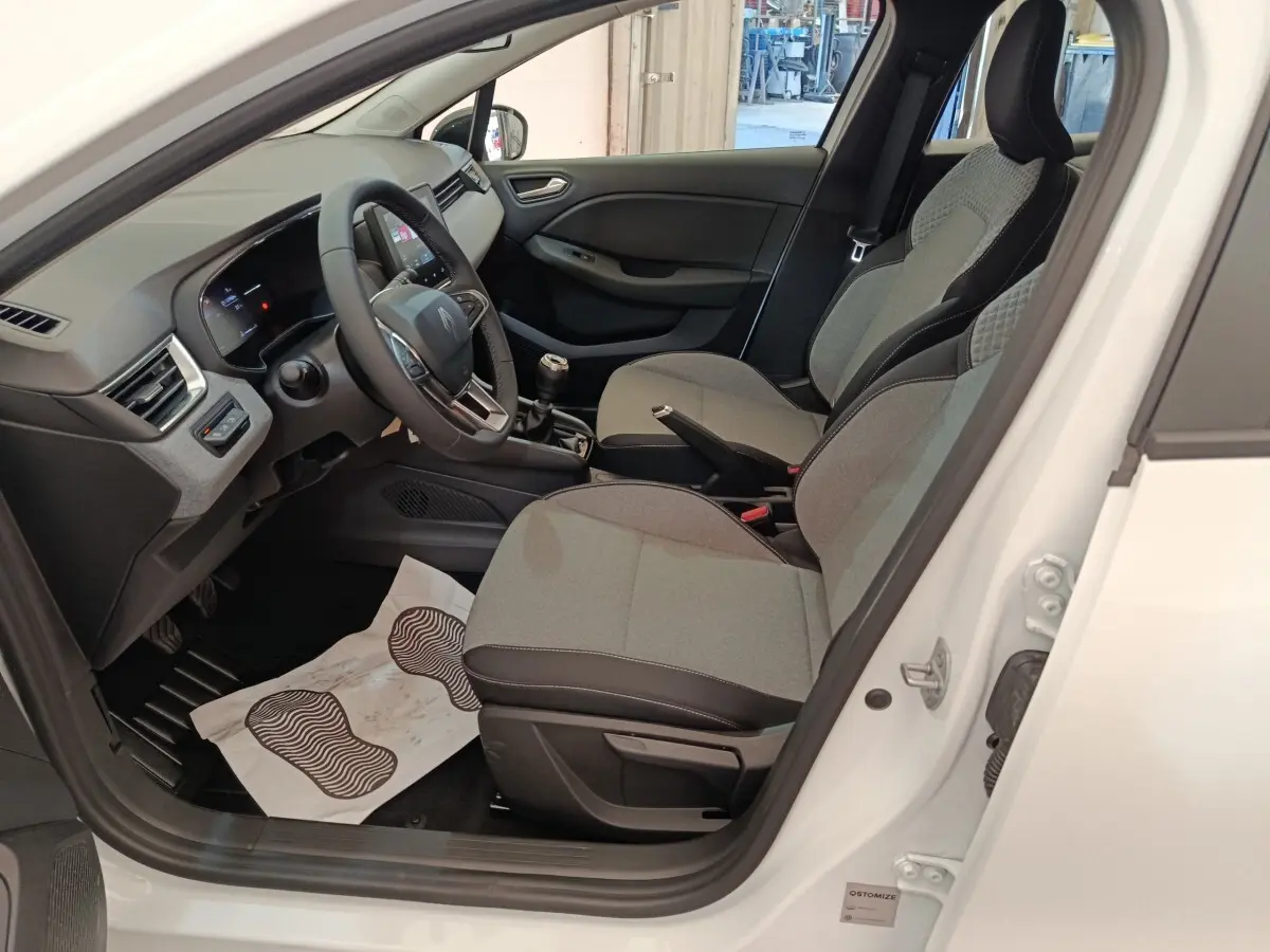 Intérieur de la Renault Clio blanche 2024 vu côté conducteur, montrant sièges gris et tableau de bord moderne.
