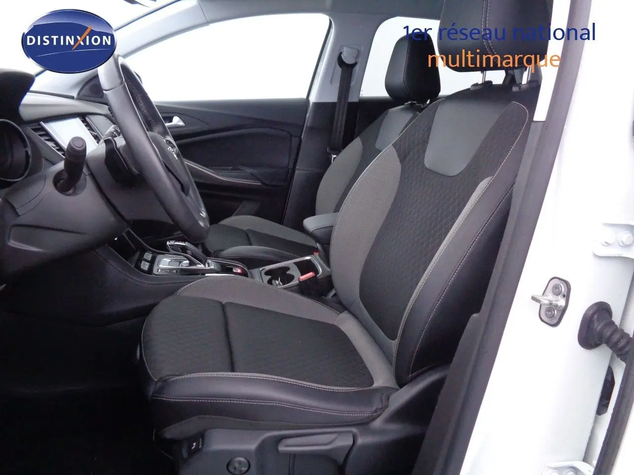 Vue intérieure côté conducteur de l’Opel Grandland X blanc métal, sièges bi-matière noir et gris avec console centrale visible.